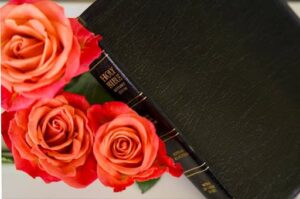 A black bible with three flowers set beside it